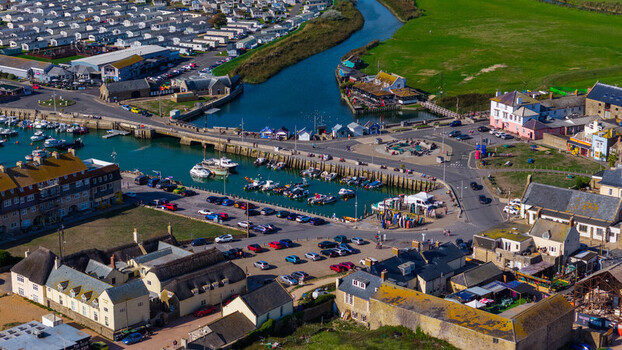 Aerial view of West Bay harbor featuring moored boats a bustling parking area and surrounding historic buildings in West Bay England United Kingdom. Aerial view of West Bay harbor featuring moored boats a bustling parking area and surrounding historic buildings in West Bay England United Kingdom.