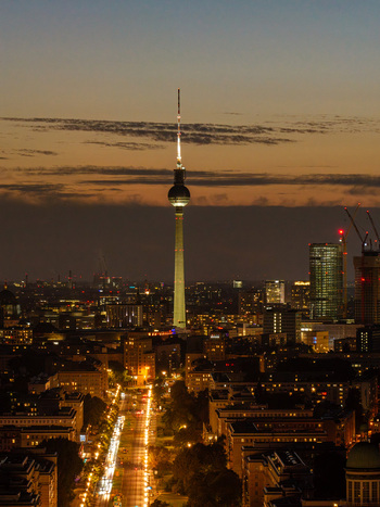 Aerial view of the illuminated Berlin TV Tower rising above the city skyline at dusk with street lights along Frankfurter Allee and urban buildings in Berlin Berlin Germany. Aerial view of the illuminated Berlin TV Tower rising above the city skyline at dusk with street lights along Frankfurter Allee and urban buildings in Berlin Berlin Germany.