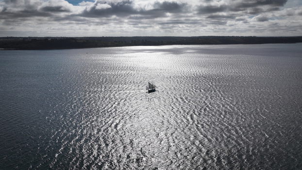 Aerial view of a lone sailboat glides across the shimmering waters reflecting sunlight amidst the coastal landscape Carantec Finistre France. Aerial view of a lone sailboat glides across the shimmering waters reflecting sunlight amidst the coastal landscape Carantec Finistre France.