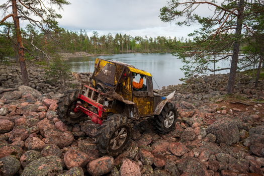 View of a muddy yellow off road vehicle navigating over large boulders near the shore of Lake Ladoga in a forest setting in Sortavala Respublika Kareliya Russia.