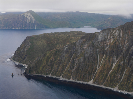 Aerial view of the rugged coastline and steep mountains of Unalaska featuring dark rocky cliffs deep blue waters and a cloudy sky in Unalaska Alaska United States.