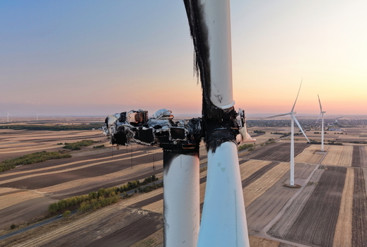 Aerial view of a burnt and damaged wind turbine nacelle with charred blades standing in agricultural fields during golden hour in Vladimirovac Vojvodina Serbia.