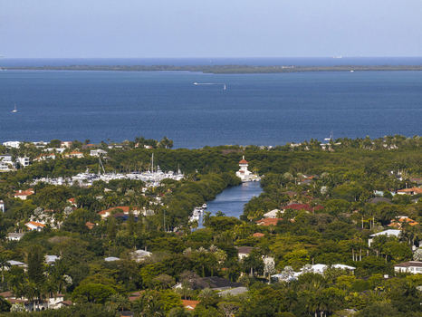 Aerial view of a coastal waterway and marina surrounded by lush tropical greenery and luxury residential homes overlooking the blue ocean in Coral Gables Florida United States.