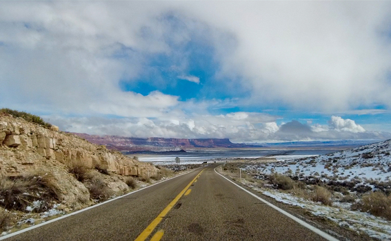 View of a long road stretching into the distance under a partly cloudy sky flanked by rocky terrain and sparse vegetation Winslow Arizona United States. View of a long road stretching into the distance under a partly cloudy sky flanked by rocky terrain and sparse vegetation Winslow Arizona United States.