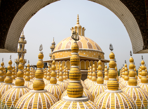 View of golden domes adorned with intricate patterns rise towards the sky framed by an ornate archway in Tangail Dhaka Division Bangladesh. View of golden domes adorned with intricate patterns rise towards the sky framed by an ornate archway in Tangail Dhaka Division Bangladesh.