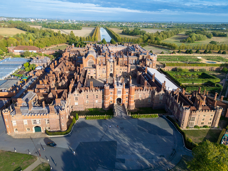 Aerial view of Hampton Court Palace showcasing its historic red brick architecture intricate courtyards and expansive surrounding gardens in Molesey England United Kingdom. Aerial view of Hampton Court Palace showcasing its historic red brick architecture intricate courtyards and expansive surrounding gardens in Molesey England United Kingdom.