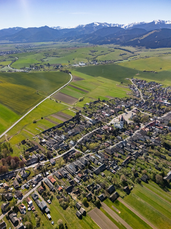 Aerial view of the historic village and church tower surrounded by green fields and snow capped mountains in Partizanska Lupca Zilina Region Slovakia.