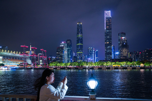 Guangzhou Guangdong Province China 22 February 2024 View of the illuminated Guangzhou skyline at night with a woman taking a photo in the foreground along the Pearl River. Guangzhou Guangdong Province China 22 February 2024 View of the illuminated Guangzhou skyline at night with a woman taking a photo in the foreground along the Pearl River.
