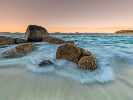 View of granite boulders on the sandy shore with turquoise ocean waves washing over the rocks under a soft sunset sky at Frenchman Bay Western Australia Australia. View of granite boulders on the sandy shore with turquoise ocean waves washing over the rocks under a soft sunset sky at Frenchman Bay Western Australia Australia.