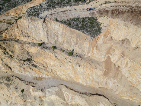 Aerial view of a limestone quarry with terraced rock faces exposed stone layers and an excavator working at the top edge in Teulada Valencian Community Spain.