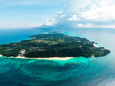 Aerial view of Boracay island featuring turquoise coral reefs white sand beaches and dense tropical forest under a clear blue sky in Malay Western Visayas Philippines.