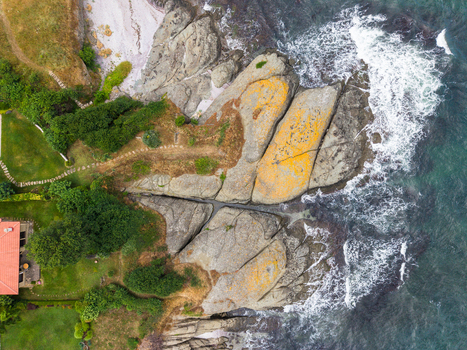 Aerial view of rocky coastline with crashing sea waves lush green grass and a house with a red roof along the shore in Lozenets Burgas Bulgaria.