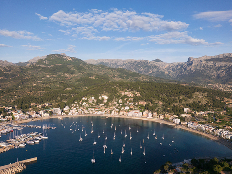 Aerial view of Port de Soller bay with sailboats anchored in calm water surrounded by coastal buildings and the Tramuntana mountains Port de Soller Balearic Islands Spain.