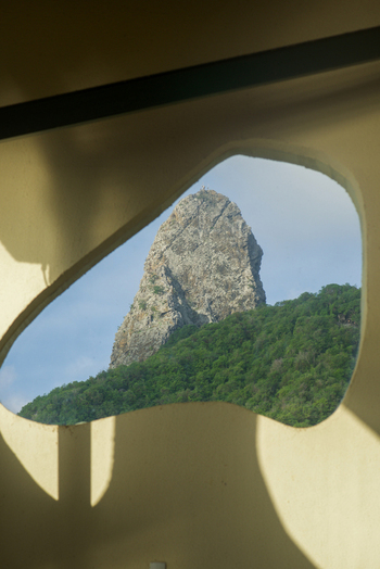 View of the Morro do Pico rock formation framed by an organic architectural opening with lush green hills under a clear sky in Fernando de Noronha State of Pernambuco Brazil. View of the Morro do Pico rock formation framed by an organic architectural opening with lush green hills under a clear sky in Fernando de Noronha State of Pernambuco Brazil.