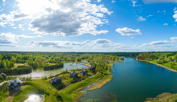 Aerial view of wooden houses nestled along a serene lake surrounded by lush green forests and rolling hills under a bright blue sky in Cesis Cesis Municipality Latvia. Aerial view of wooden houses nestled along a serene lake surrounded by lush green forests and rolling hills under a bright blue sky in Cesis Cesis Municipality Latvia.
