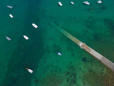 Aerial view of Plage de Port Blanc featuring a stone pier extending into turquoise waters with small boats anchored nearby in Penvenan Bretagne France. Aerial view of Plage de Port Blanc featuring a stone pier extending into turquoise waters with small boats anchored nearby in Penvenan Bretagne France.