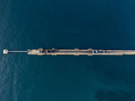 Aerial view of a long industrial pier extending into the deep blue sea featuring metallic structures and machinery in Bajos de Haina San Cristobal Provinc Dominican Republic.