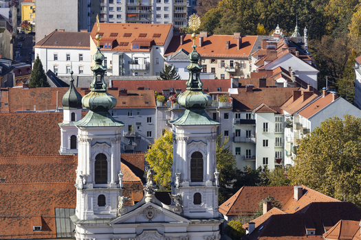 View of church towers rise amidst a sea of terracotta rooftops set against a backdrop of modern buildings and autumn foliage Graz Styria Austria. View of church towers rise amidst a sea of terracotta rooftops set against a backdrop of modern buildings and autumn foliage Graz Styria Austria.