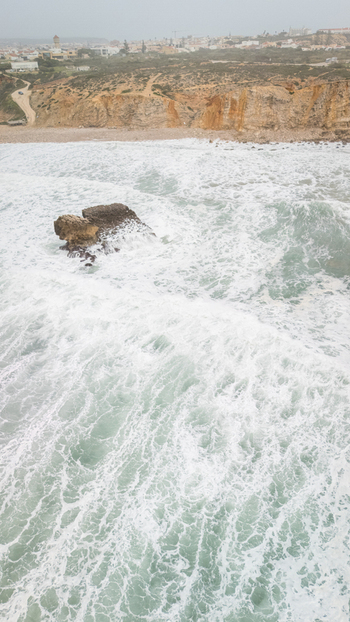 Aerial view of rough Atlantic waves crashing against a rock formation and steep cliffs near the town of Sagres Faro Portugal. Aerial view of rough Atlantic waves crashing against a rock formation and steep cliffs near the town of Sagres Faro Portugal.