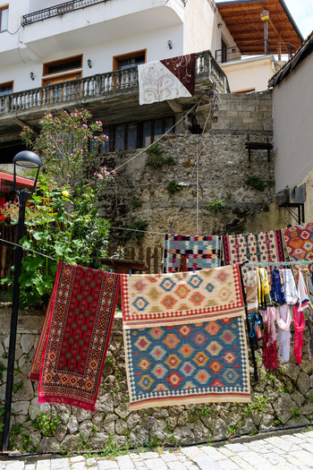 View of traditional colorful handmade carpets and rugs hanging on a clothesline against a stone wall and historic buildings in Kruje Durres County Albania.