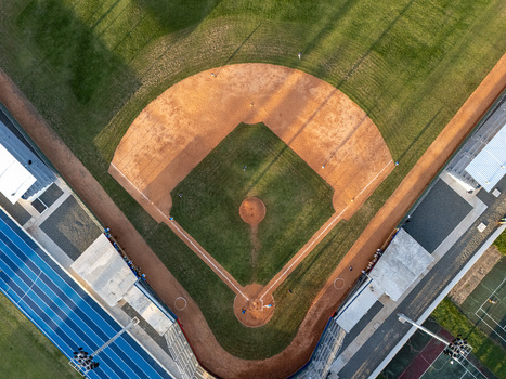 Aerial view of a baseball field with a dirt infield and green outfield grass featuring stadium lights and adjacent blue running track in Santo Domingo Distrito Nacional Dominican Republic.