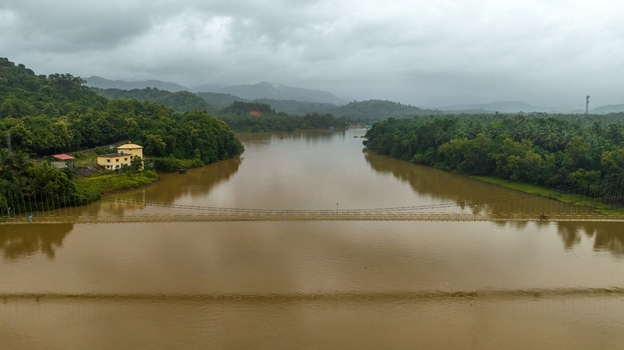 Aerial view of the suspension bridge spanning the Sharavathi River surrounded by lush green vegetation and hills under a cloudy sky in Honnavar Karnataka India.