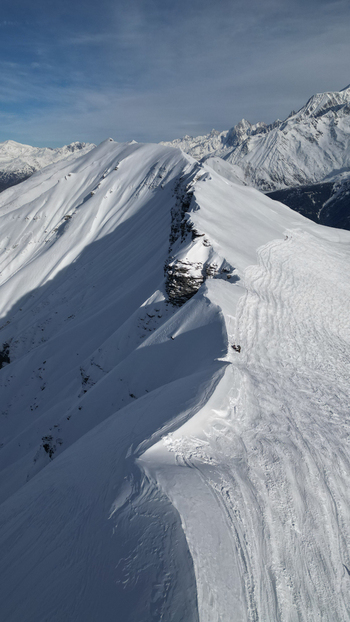 Aerial view of Aiguille Croche mountain ridge covered in deep snow with ski tracks under a clear blue sky in Les Contamines Montjoie Auvergne Rhone Alpes France. Aerial view of Aiguille Croche mountain ridge covered in deep snow with ski tracks under a clear blue sky in Les Contamines Montjoie Auvergne Rhone Alpes France.