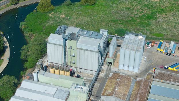 Aerial view of a large industrial mill facility featuring tall storage silos and warehouse buildings situated next to a river in Little Irchester England United Kingdom. Aerial view of a large industrial mill facility featuring tall storage silos and warehouse buildings situated next to a river in Little Irchester England United Kingdom.
