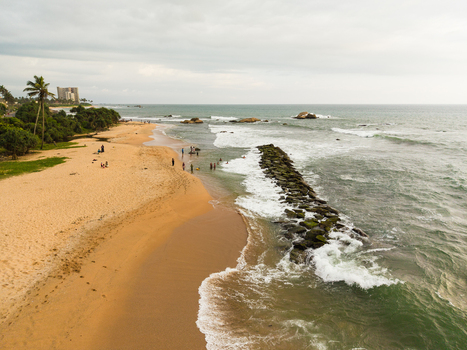 Aerial view of Dadalla beach featuring a stone breakwater people on the sand and waves crashing on the shore in Galle Southern Province Sri Lanka. Aerial view of Dadalla beach featuring a stone breakwater people on the sand and waves crashing on the shore in Galle Southern Province Sri Lanka.