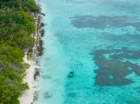 Aerial view of a lone boat adrift in the turquoise waters contrasting with the verdant shoreline of Vashafaru Island Vashafaru Island Thiladhummathi Atoll Maldives. Aerial view of a lone boat adrift in the turquoise waters contrasting with the verdant shoreline of Vashafaru Island Vashafaru Island Thiladhummathi Atoll Maldives.