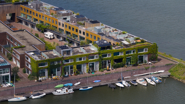 Aerial view of sustainable housing with green facades and rooftop gardens along a canal with moored boats in Amsterdam North Holland Netherlands. Aerial view of sustainable housing with green facades and rooftop gardens along a canal with moored boats in Amsterdam North Holland Netherlands.