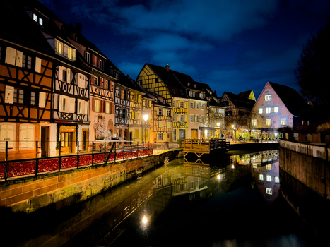 View of the historic half timbered houses along the canal in Little Venice at night with warm lights reflecting on the water in Colmar Grand Est France.