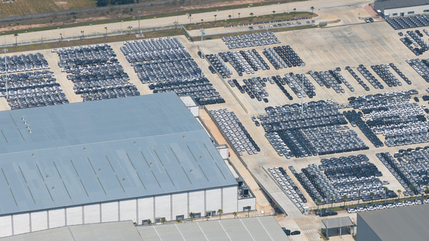 Aerial view of BYD AUTO THAILAND CO. LTD. factory with thousands of new electric vehicles parked in neat rows next to large industrial warehouses in Phananikhom Rayong Thailand.