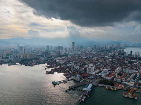 Aerial view of the historic waterfront jetties and modern skyline of George Town under a dramatic cloudy sky in George Town Penang Malaysia. Aerial view of the historic waterfront jetties and modern skyline of George Town under a dramatic cloudy sky in George Town Penang Malaysia.