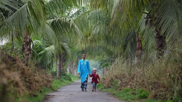 View of a man and child walking on a path with palm trees Bangladesh. View of a man and child walking on a path with palm trees Bangladesh.