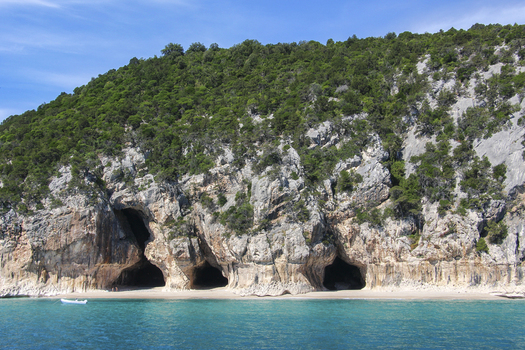 View of the sea caves along the limestone cliffs of the Gulf of Orosei with turquoise water and lush green vegetation in Italy. View of the sea caves along the limestone cliffs of the Gulf of Orosei with turquoise water and lush green vegetation in Italy.