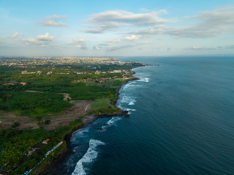 Aerial view of the coastline of Kediri featuring lush green vegetation rocky cliffs and waves crashing against the shore under a clear blue sky Kediri Bali Indonesia.