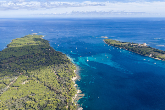 Aerial view of Ile Sainte Marguerite with dense forest and historic fort surrounded by turquoise Mediterranean waters and anchored sailboats near Cannes Provence Alpes Cote d Azur France. Aerial view of Ile Sainte Marguerite with dense forest and historic fort surrounded by turquoise Mediterranean waters and anchored sailboats near Cannes Provence Alpes Cote d Azur France.