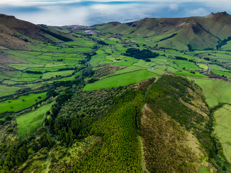 Aerial view of the vibrant green pastures and rolling hills stretching towards the distant coastline Lake Comprida Flores Azores Portugal.