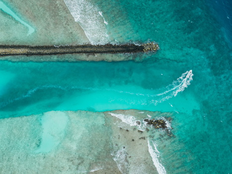 Aerial view of a boat cutting through the turquoise channel bordered by a stone barrier and shallow reefs Vashafaru Island Thiladhummathi Atoll Maldives. Aerial view of a boat cutting through the turquoise channel bordered by a stone barrier and shallow reefs Vashafaru Island Thiladhummathi Atoll Maldives.