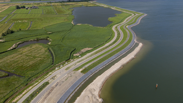 Aerial view of the dike reinforcement project along the coastline with a winding road green embankments and sandy construction works in Uitdam North Holland Netherlands.