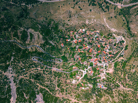 Aerial view of the historic stone houses and red tiled roofs of Qeparo Fshat village nestled on a green hillside with winding mountain roads in Qeparo Fshat Vlore County Albania. Aerial view of the historic stone houses and red tiled roofs of Qeparo Fshat village nestled on a green hillside with winding mountain roads in Qeparo Fshat Vlore County Albania.