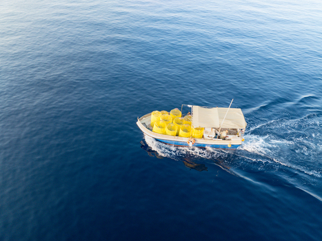 Aerial view of a small boat cuts through the deep blue sea its wake a frothy contrast loaded with yellow containers against a white canopy Ghajnsielem Gozo Malta. Aerial view of a small boat cuts through the deep blue sea its wake a frothy contrast loaded with yellow containers against a white canopy Ghajnsielem Gozo Malta.