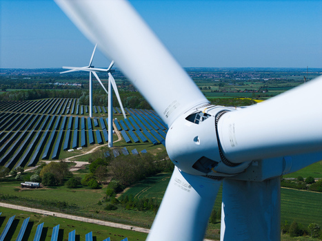 Aerial view of Chelveston Wind Farm featuring wind turbines and solar panels across green fields under a clear blue sky in Wellingborough England United Kingdom. Aerial view of Chelveston Wind Farm featuring wind turbines and solar panels across green fields under a clear blue sky in Wellingborough England United Kingdom.