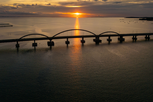 Aerial view of the arched bridge over the sea at sunset with golden light reflecting on the water near Bintan Island Tanjung Pinang Riau Islands Indonesia. Aerial view of the arched bridge over the sea at sunset with golden light reflecting on the water near Bintan Island Tanjung Pinang Riau Islands Indonesia.