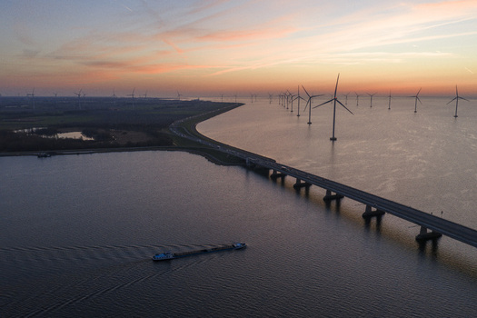 Aerial view of the Ketelbrug bridge crossing the water with offshore wind turbines and a cargo ship under a sunset sky in Nagele Flevoland Netherlands.