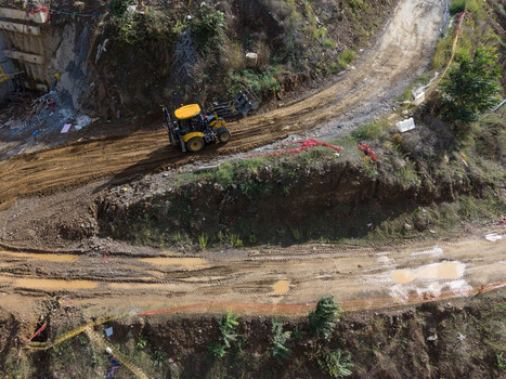 Aerial view of a yellow backhoe loader working on a muddy dirt road at a construction site with excavated earth and sparse vegetation in Istanbul Istanbul Turkiye. Aerial view of a yellow backhoe loader working on a muddy dirt road at a construction site with excavated earth and sparse vegetation in Istanbul Istanbul Turkiye.