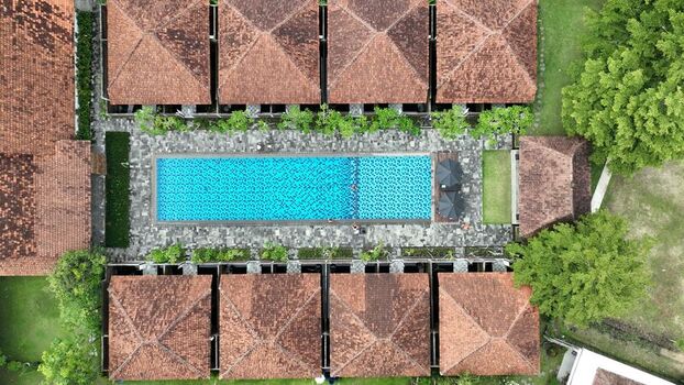 Aerial view of a luxury resort with a blue swimming pool and traditional brown tiled roofs surrounded by lush greenery in Borobudur Central Java Indonesia. Aerial view of a luxury resort with a blue swimming pool and traditional brown tiled roofs surrounded by lush greenery in Borobudur Central Java Indonesia.