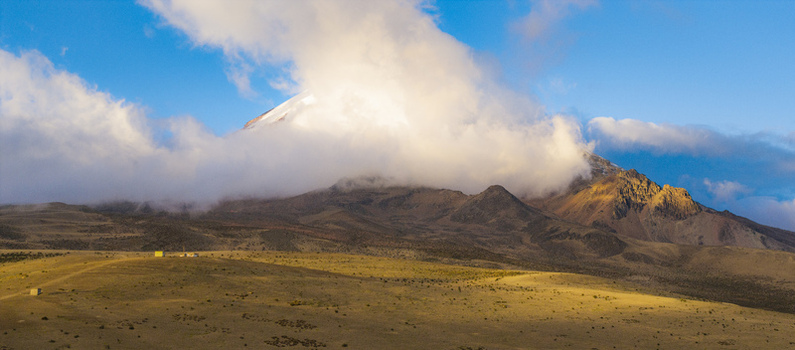 Aerial view of Volcano Chimborazo with its snow capped peak partially obscured by clouds rising above the arid golden hued landscape in Guano Chimborazo Ecuador. Aerial view of Volcano Chimborazo with its snow capped peak partially obscured by clouds rising above the arid golden hued landscape in Guano Chimborazo Ecuador.