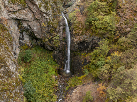 Aerial view of Ovcharenski Waterfall Goritsa cascading down a rocky cliff face surrounded by lush autumn foliage and dense forest in Ovchartsi Kyustendil Province Bulgaria. Aerial view of Ovcharenski Waterfall Goritsa cascading down a rocky cliff face surrounded by lush autumn foliage and dense forest in Ovchartsi Kyustendil Province Bulgaria.
